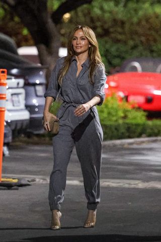 Jennifer Lopez walking in a parking lot wearing a jumpsuit and high heels