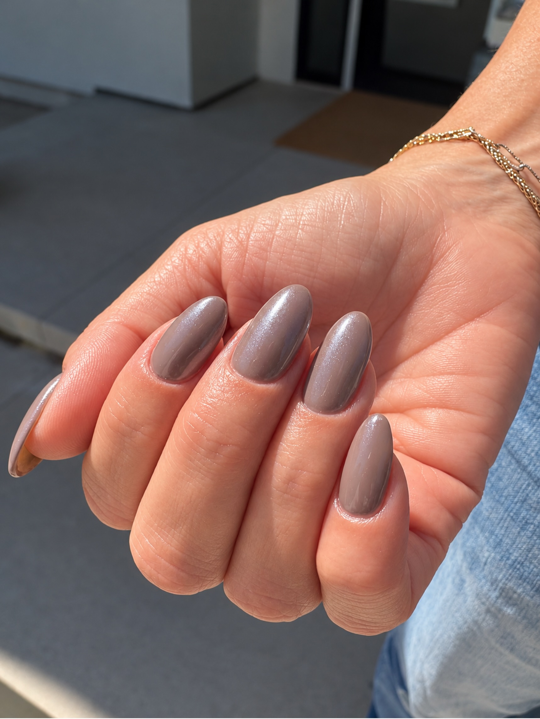 muted grayish brown nails with a frosty chrome finish, hand held out against a dark background