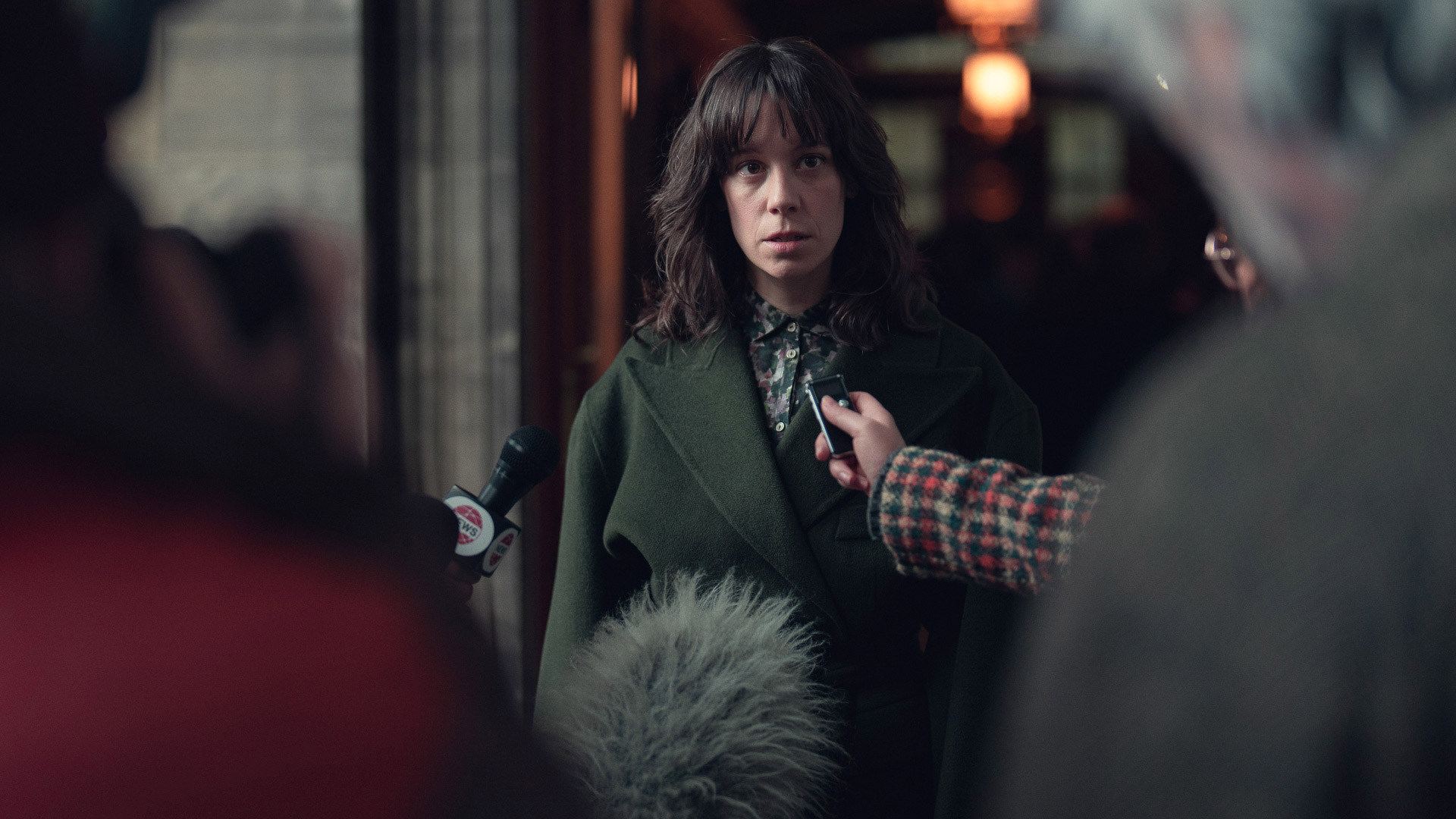 A still from episode 6 of Dept Q featuring a woman being interviewed by the press