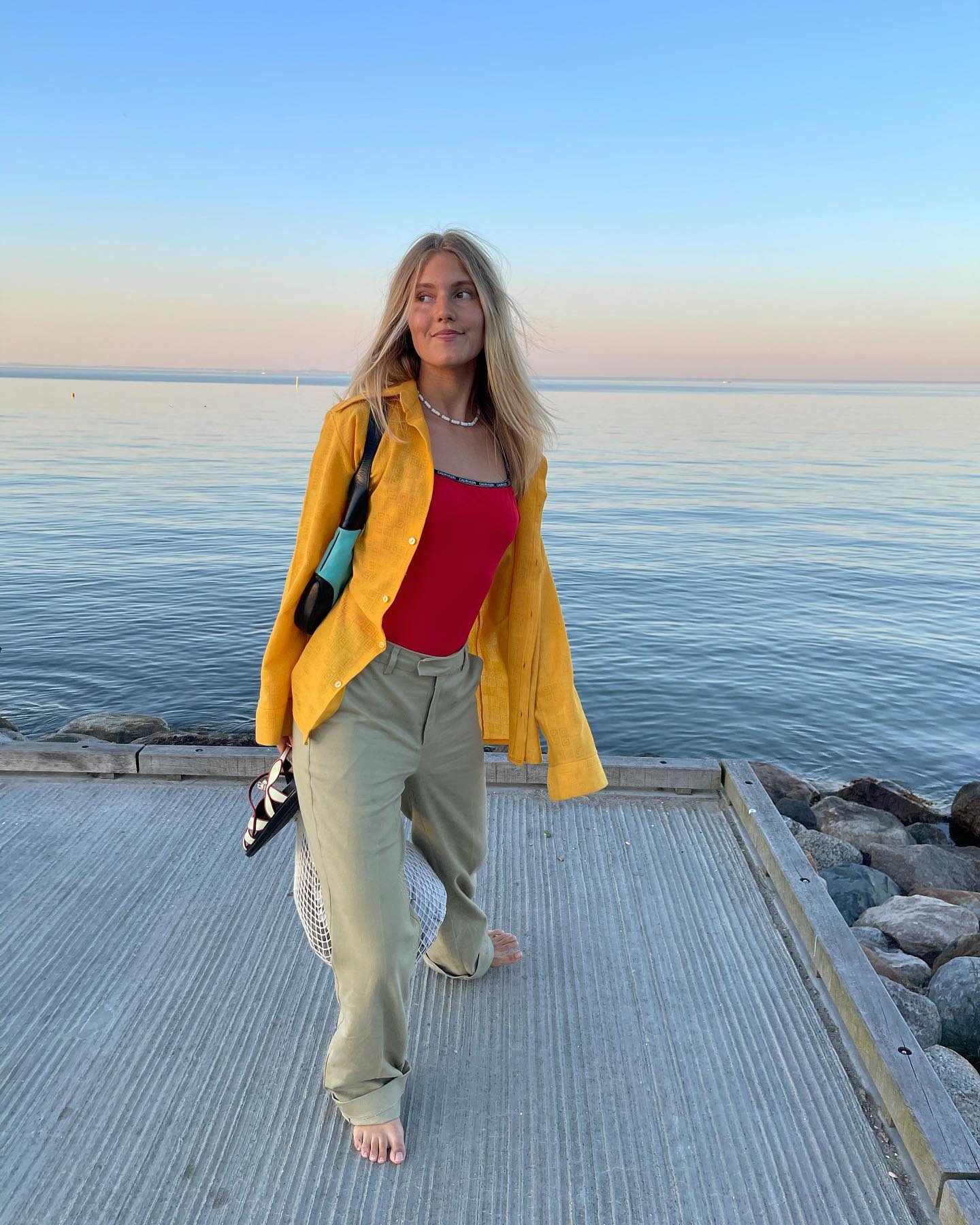 Anna wears an orange button-down shirt, red bathing suit, and khaki pants.