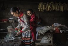 A woman of the Long Horn Miao ethnic minority group carries a baby on her back as she cooks after Tiaohua or Flower Festival as part of the Lunar New Year in Xiaobatian village, China.