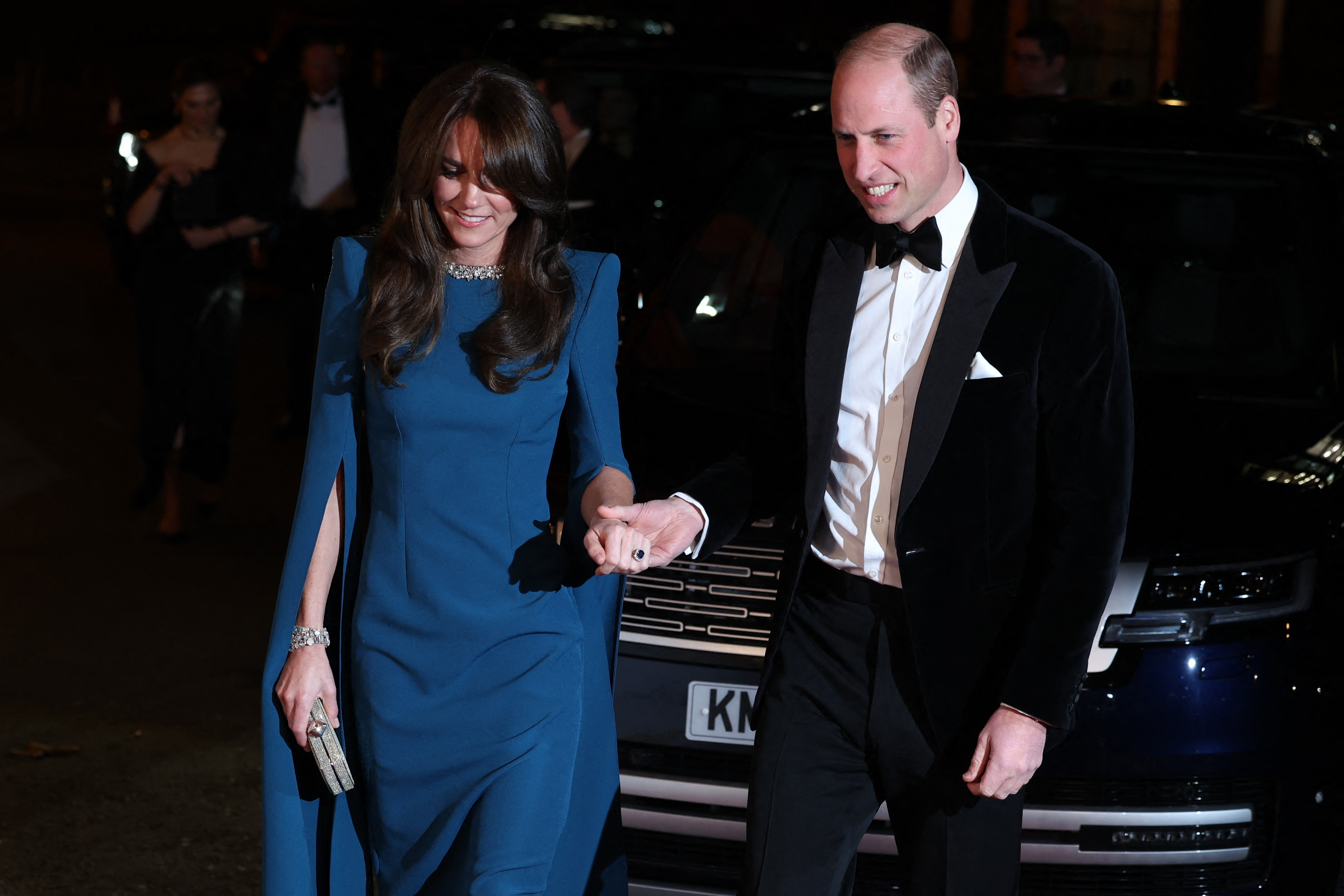 Kate Middleton wearing a blue gown holding hands with Prince William, dressed in a tuxedo