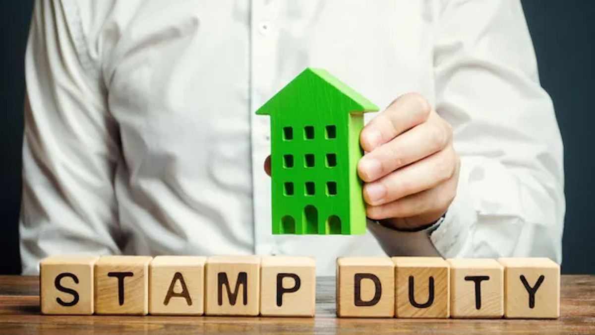 A man holding a toy house over wooden blocks that spell out STAMP DUTY