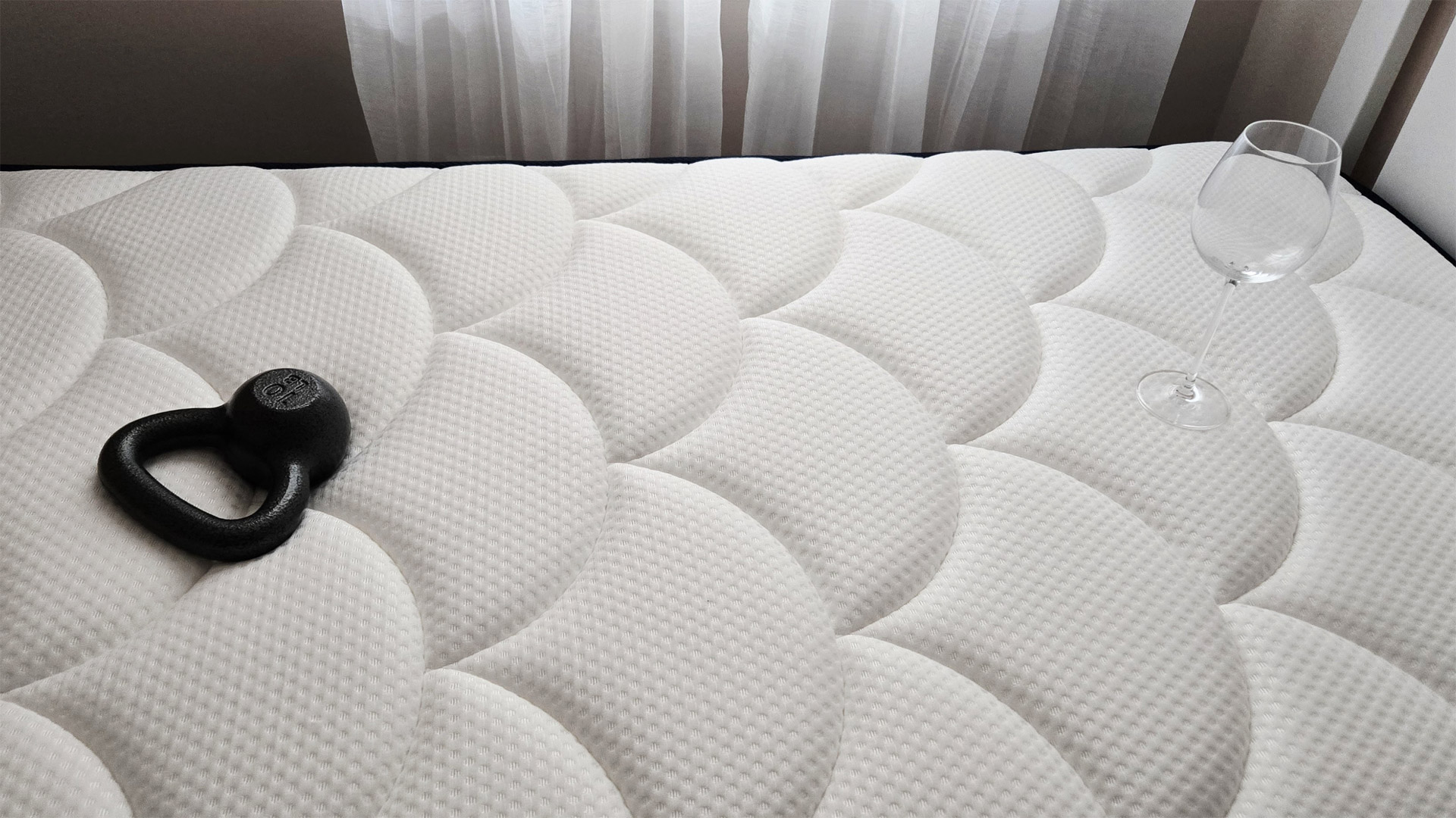 A 10lb kettlebell approximately 25&quot; away from an empty wine glass post-drop during a motion isolation test for the DreamCloud Classic Memory Foam Mattress review