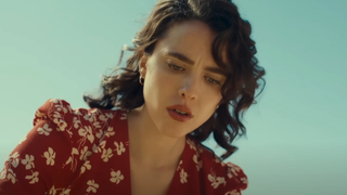 Margaret Qualley looking down in red blouse in Honey Don't