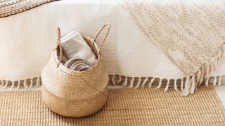 Folded gray knitted plaid in straw basket on wicker carpet near bed