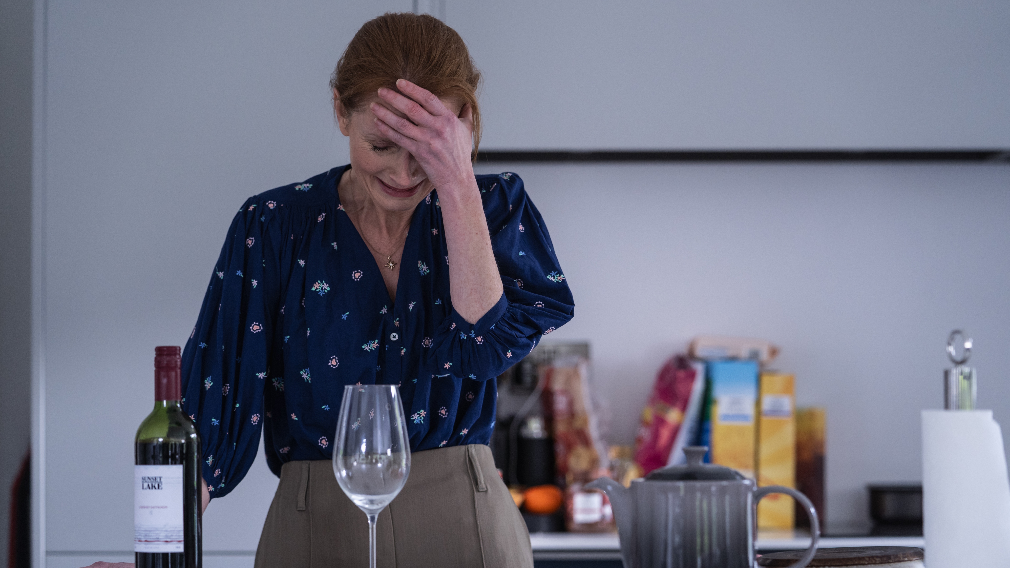Kate looking upset as she pours red wine in her kicthen