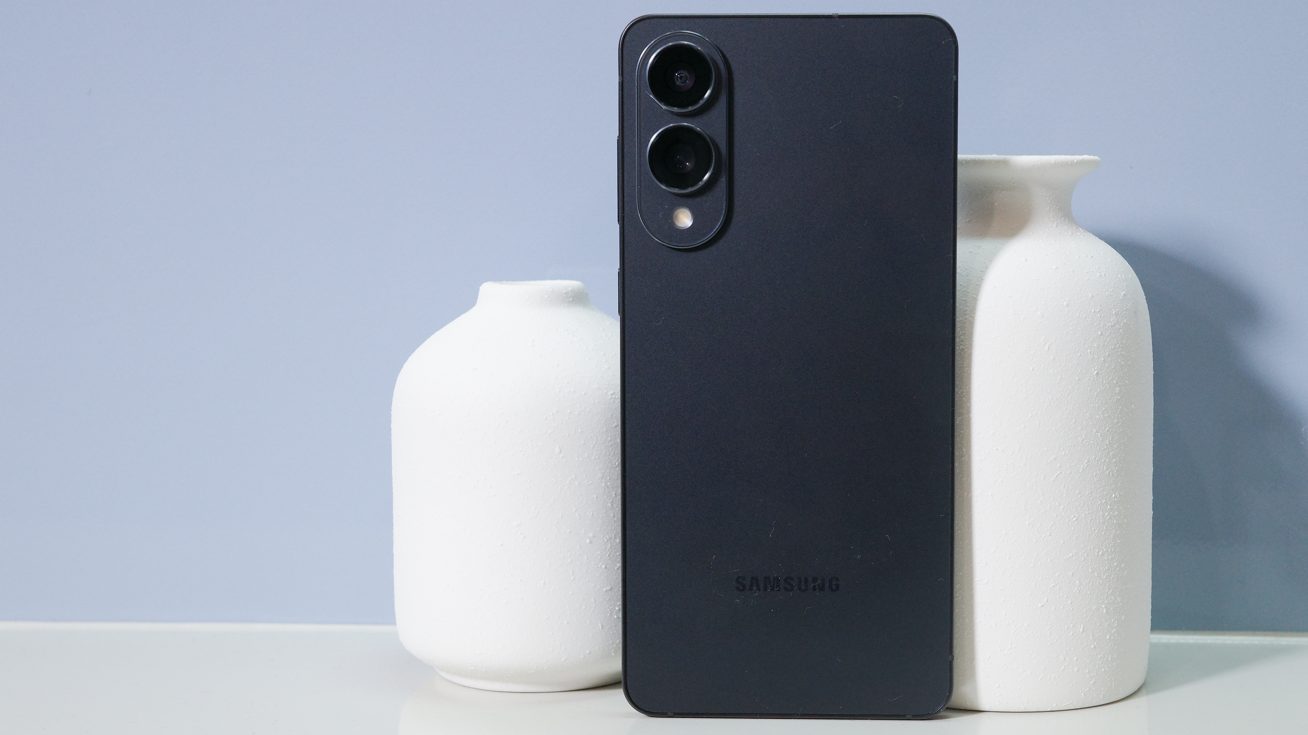 Samsung Galaxy S25 Edge in black against a blue background with two white vases