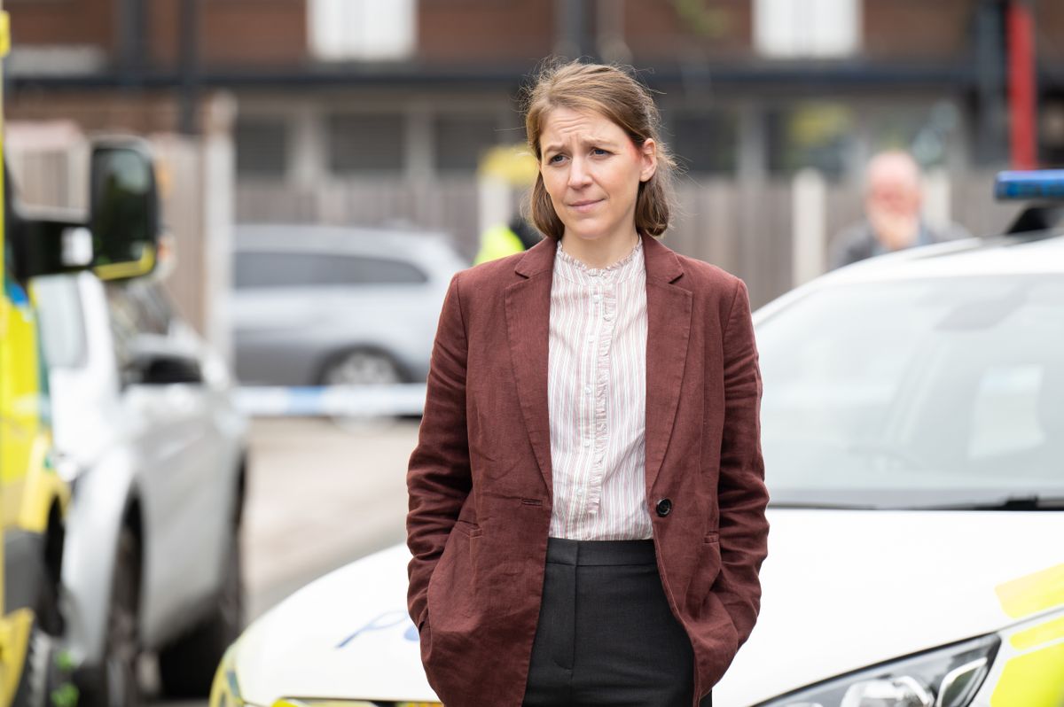 Sarah Collins standing with her hands in her pockets with police cars behind her.