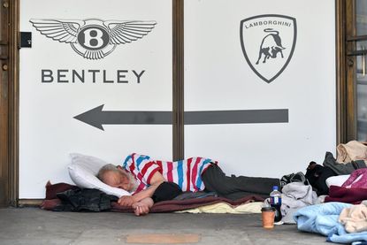 Homeless man sleeps in front of a luxury car dealership