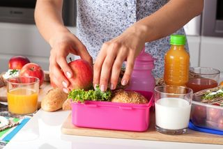 A woman makes a lunch in a lunch box.