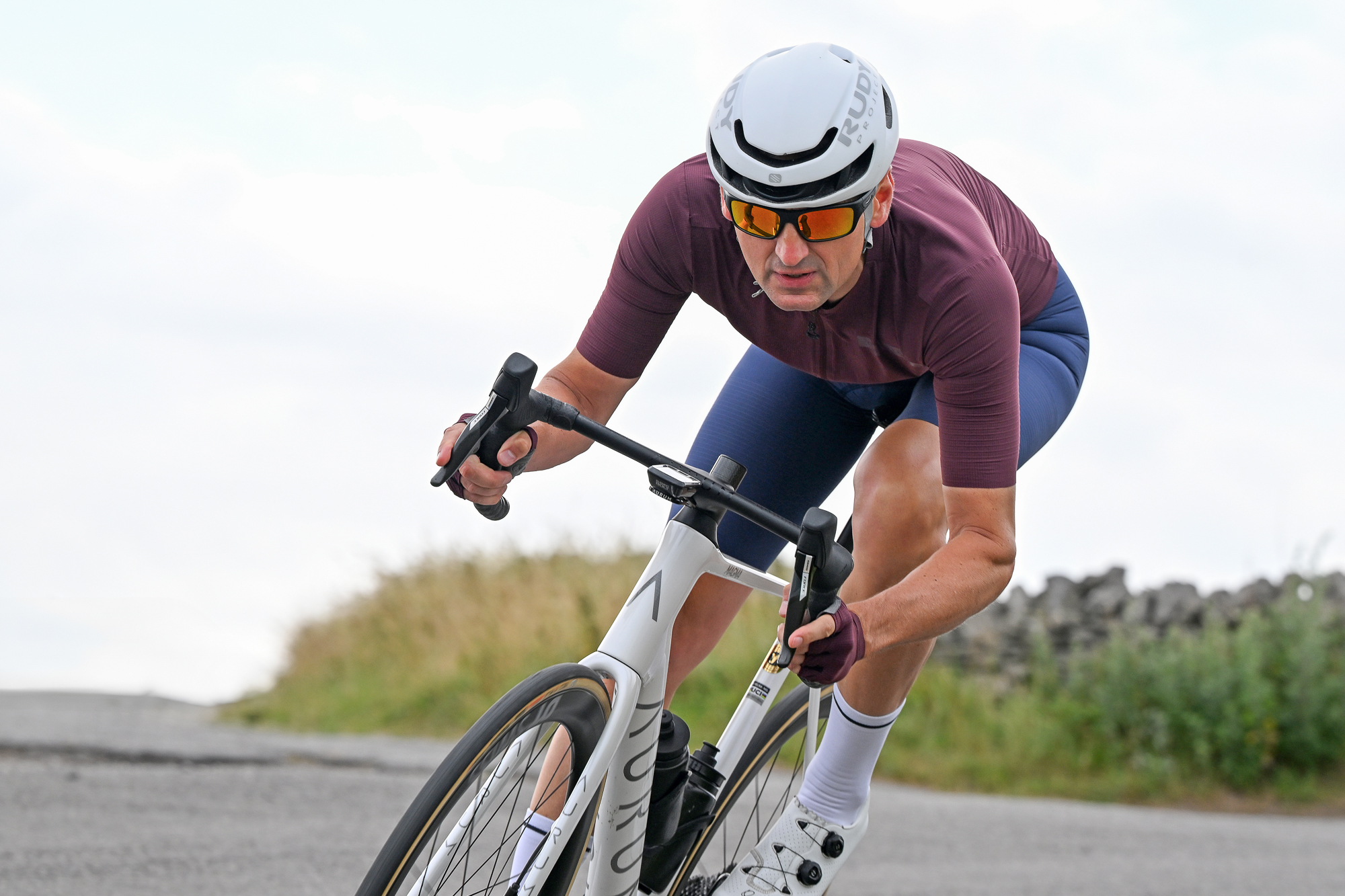 man riding a white bike downhill wearing a purple jersey, purple gloves, blue shorts and a white helmet