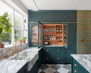 Cozy kitchen with blue painted cabinets, marble counters and dark floral wallpaper