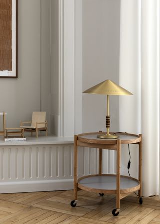 A brown tray table with two circular shelves. The top shelf has a gold coloured lamp standing on it.