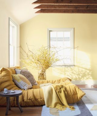 Benjamin Moore's pale moon pain - a pasyel yello - on one wall of a bedroom, a bed with bright yellow bedding, and yellow flowers