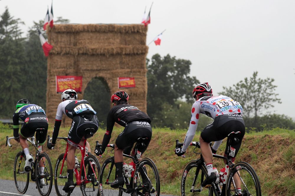 Vegard Breen, Jasper Stuyven, Cesare Benedetti and Paul Voss, wearing the best climber's polka dot jersey, ride in a breakaway past an arc of triumph made with straw during the 183 km second stage of the 103rd edition of the Tour de France