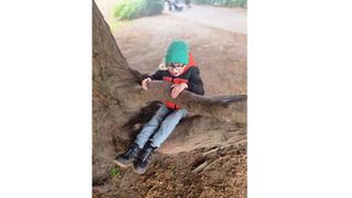 Boy in red coat and green hat sat on tree