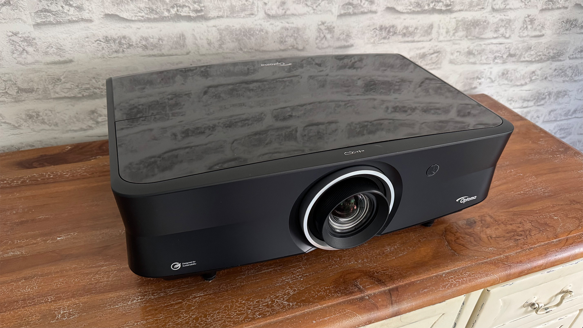 Optoma UHZ68LV home cinema projector on wooden sideboard in front of grey brick wall