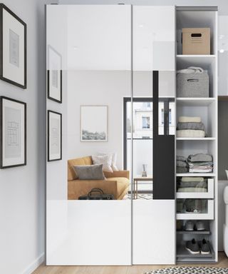 A mirror fronted wardrobe with storage shelves reflecting a room with a brown chair