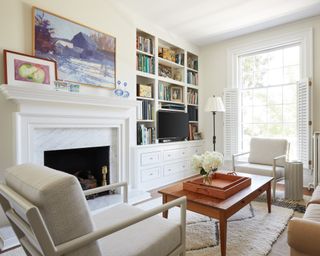 A family living room with cream walls, white woodwork, marble fireplace, white armchairs and taupe sofa