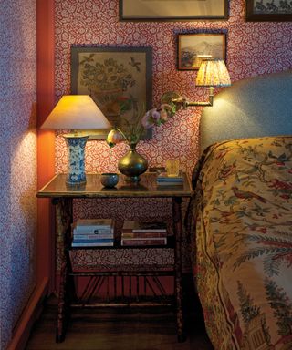 botanical red wallpaper in a bedroom, bedside table with two bedside lights, pictures on the wall, dark wooden furniture