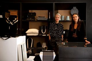 Two ladies standing behind a display unit in the store featuring monochrome interiors and accessories on display