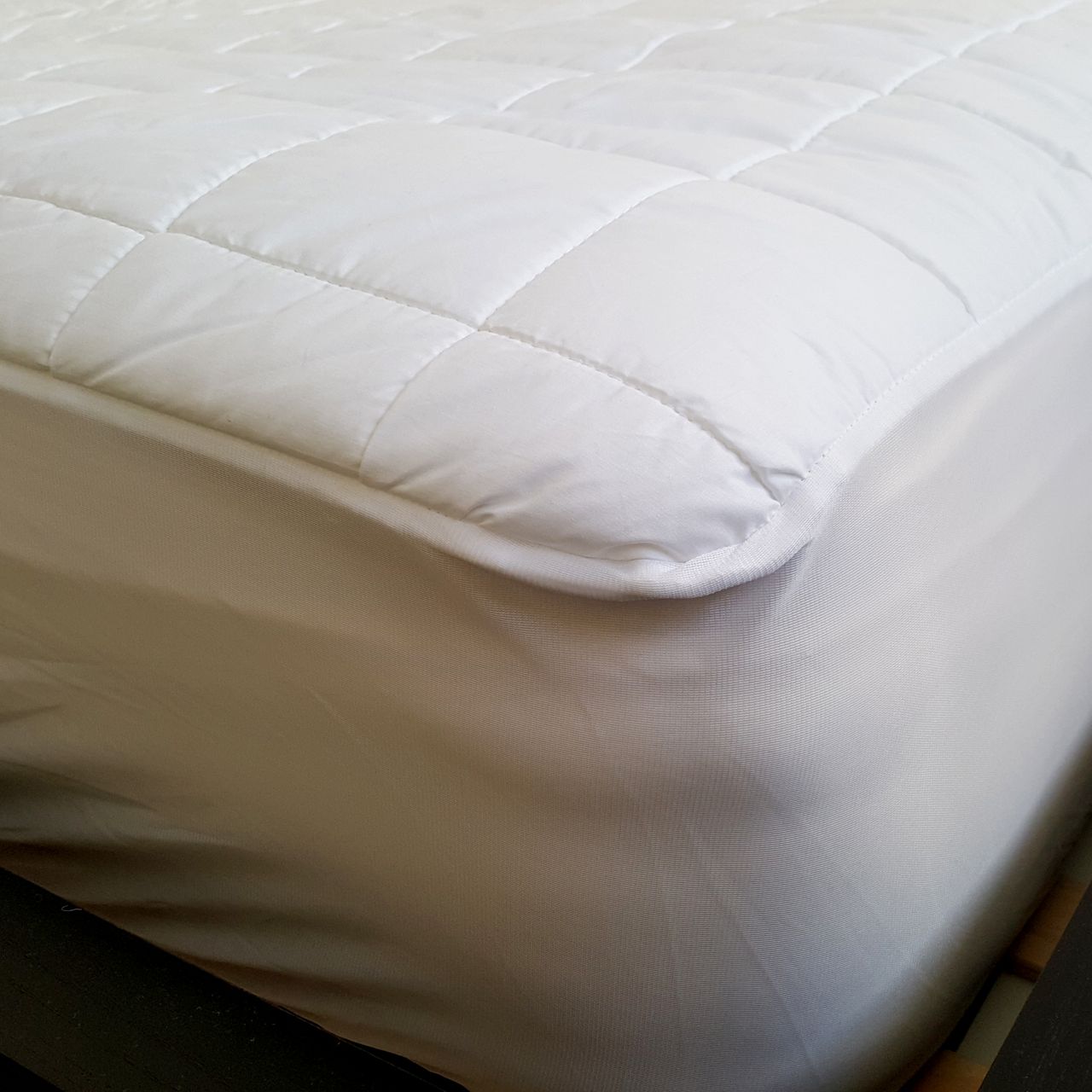 The corner of the Dreamland Snowed In Dual Control Heated Mattress Protector showing its white mesh fitted skirt