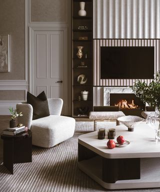 neutral living area with marble fireplace, fluted TV surround, white chair and large white shaped coffee table