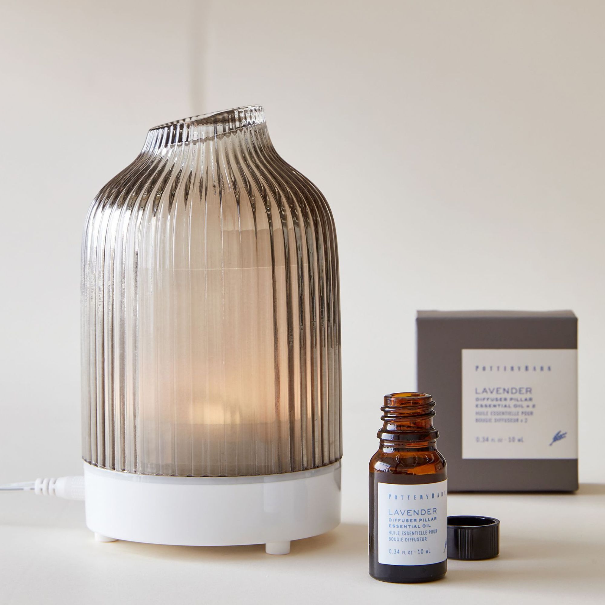 Fluted glass essential oil diffuser with white base and a small bottle of lavender oil beside it