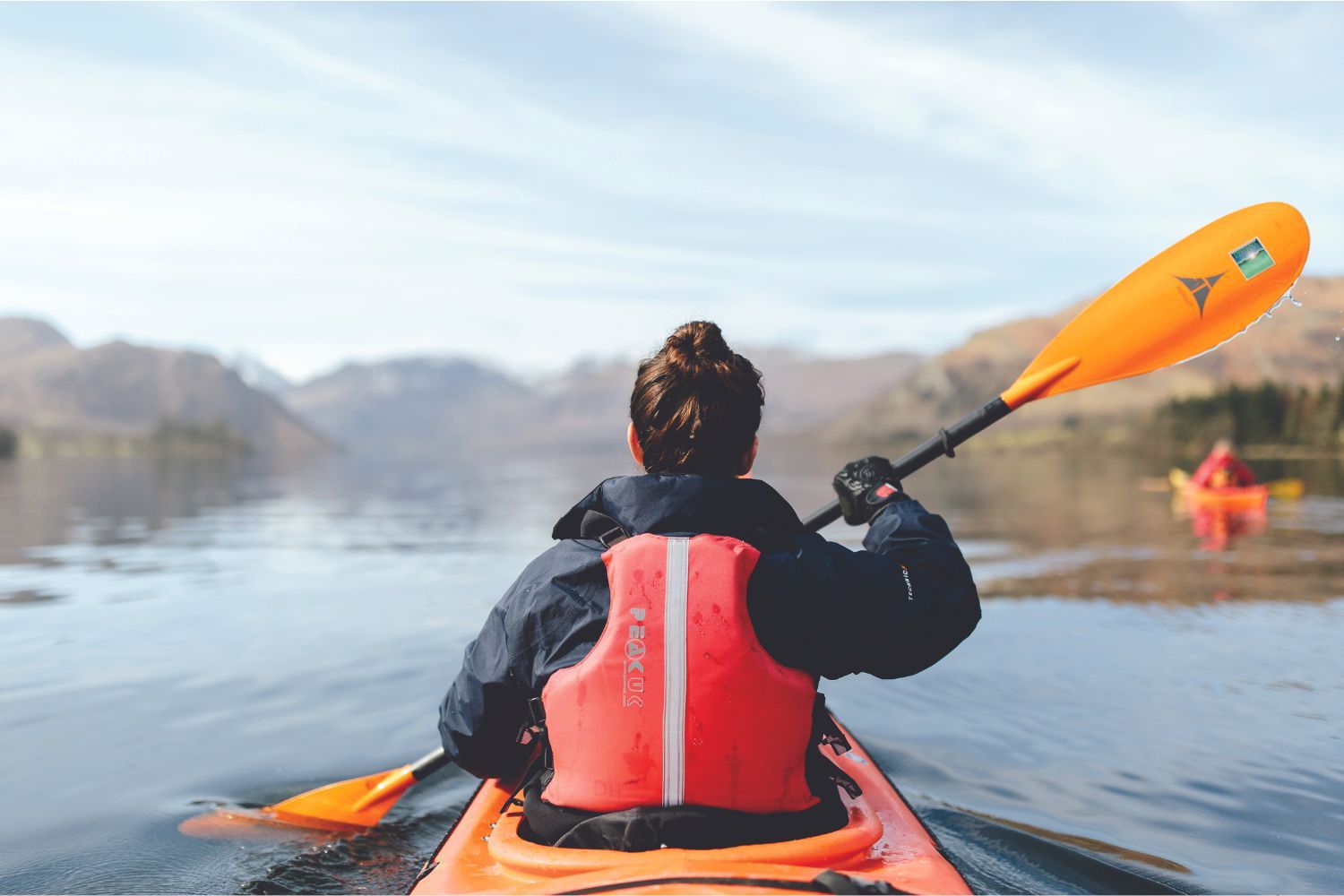 Image of a woman from behind as she is kayaking through the blue sea