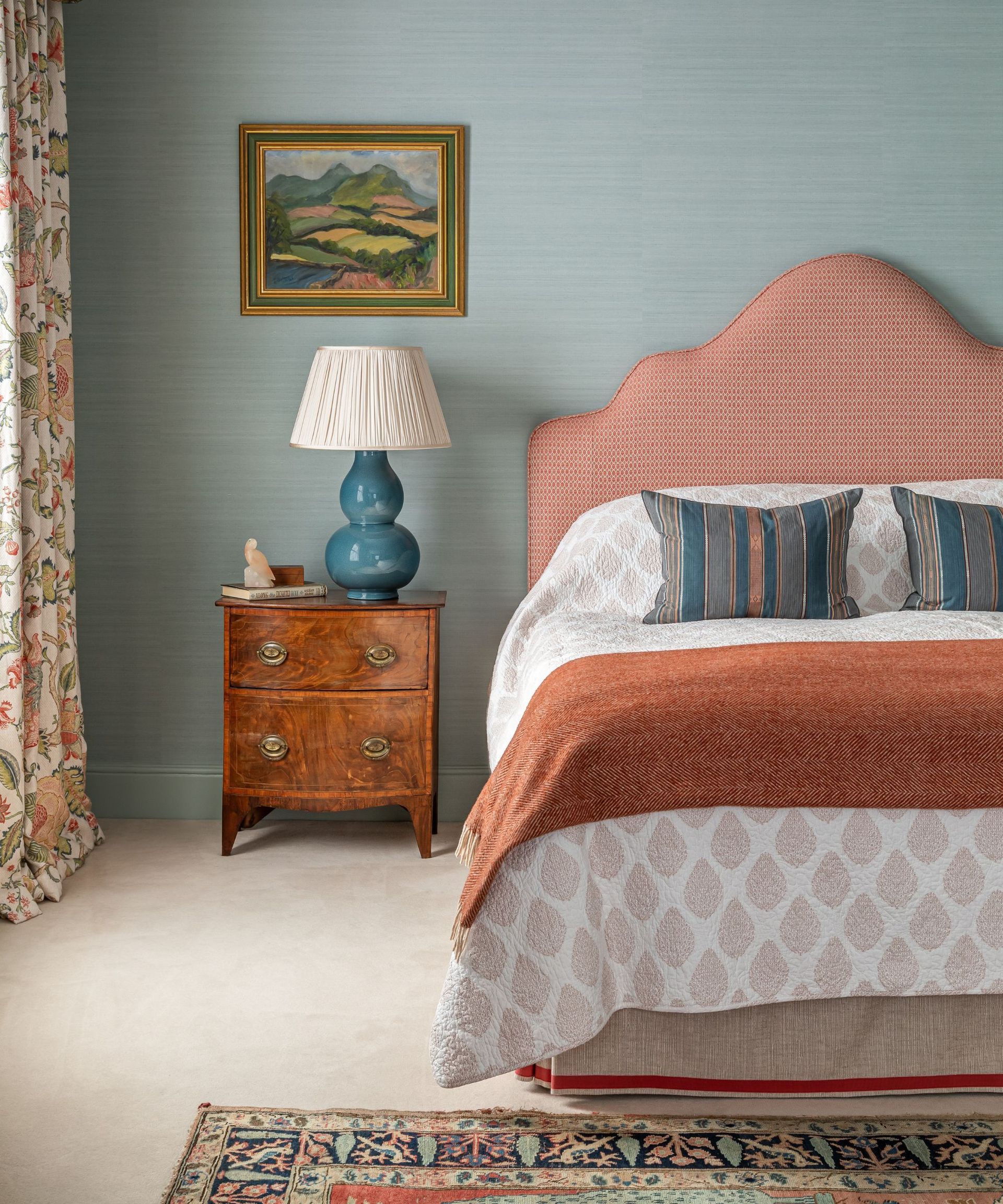 A bedroom with pale blue walls and a bed with an orange headboard and throw