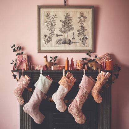 A black fireplace decorated for Christmas with pink Christmas stockings, a dried orange garland and other decor set against a pink wall