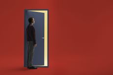 A man stands in front of a stylized blue door on a red background. The door is slightly open and he in contemplating walking through it.