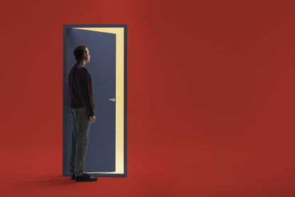 A man stands in front of a stylized blue door on a red background. The door is slightly open and he in contemplating walking through it.