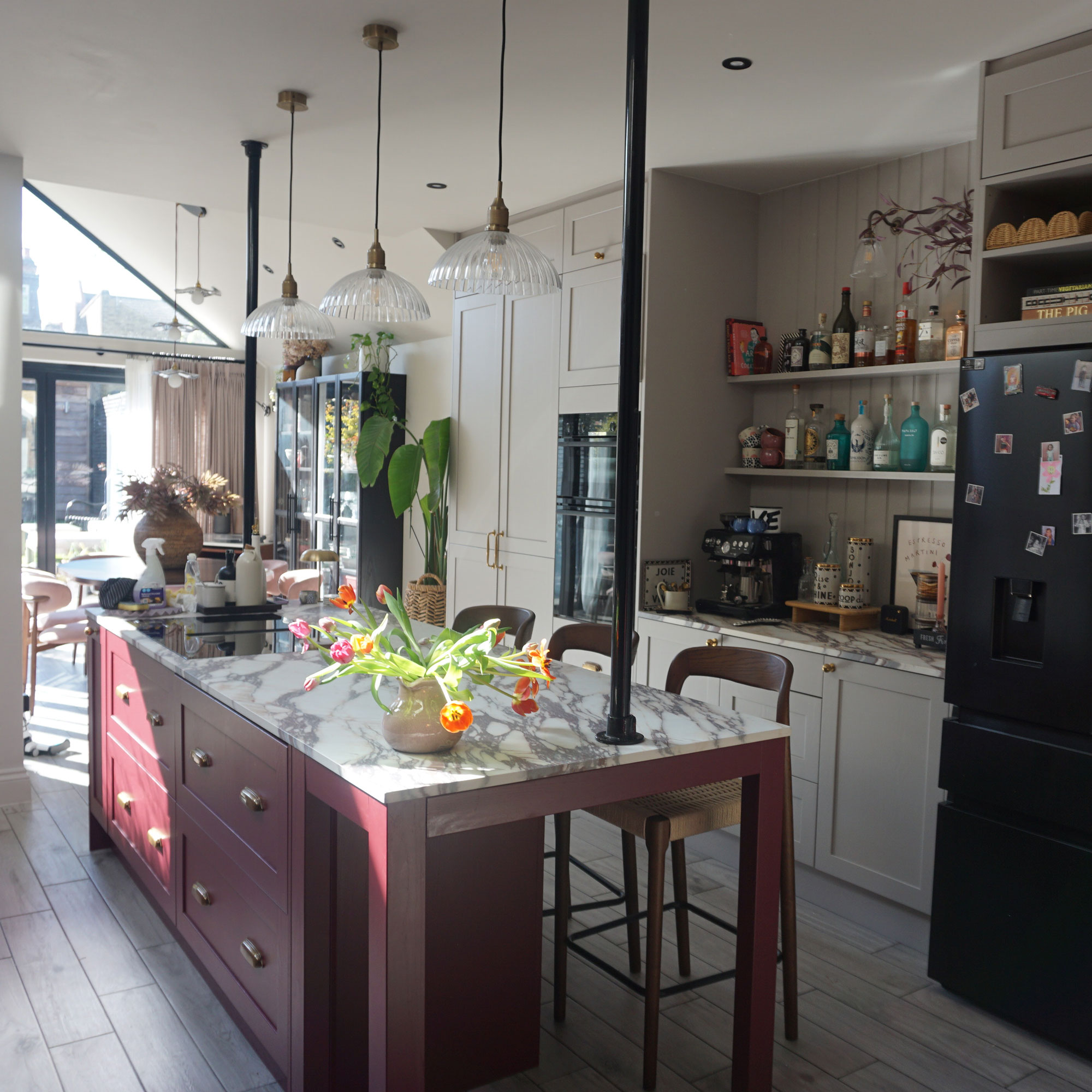 Kitchen with red and grey cabinetry, marble topped island with three glass pendant lights above