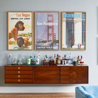 Floating wooden sideboard topped with bottles and below three vintage film posters