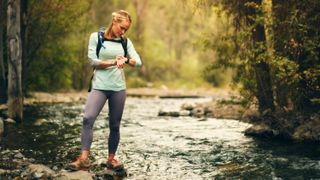 Hiker standing on rocks in stream while checking her watch