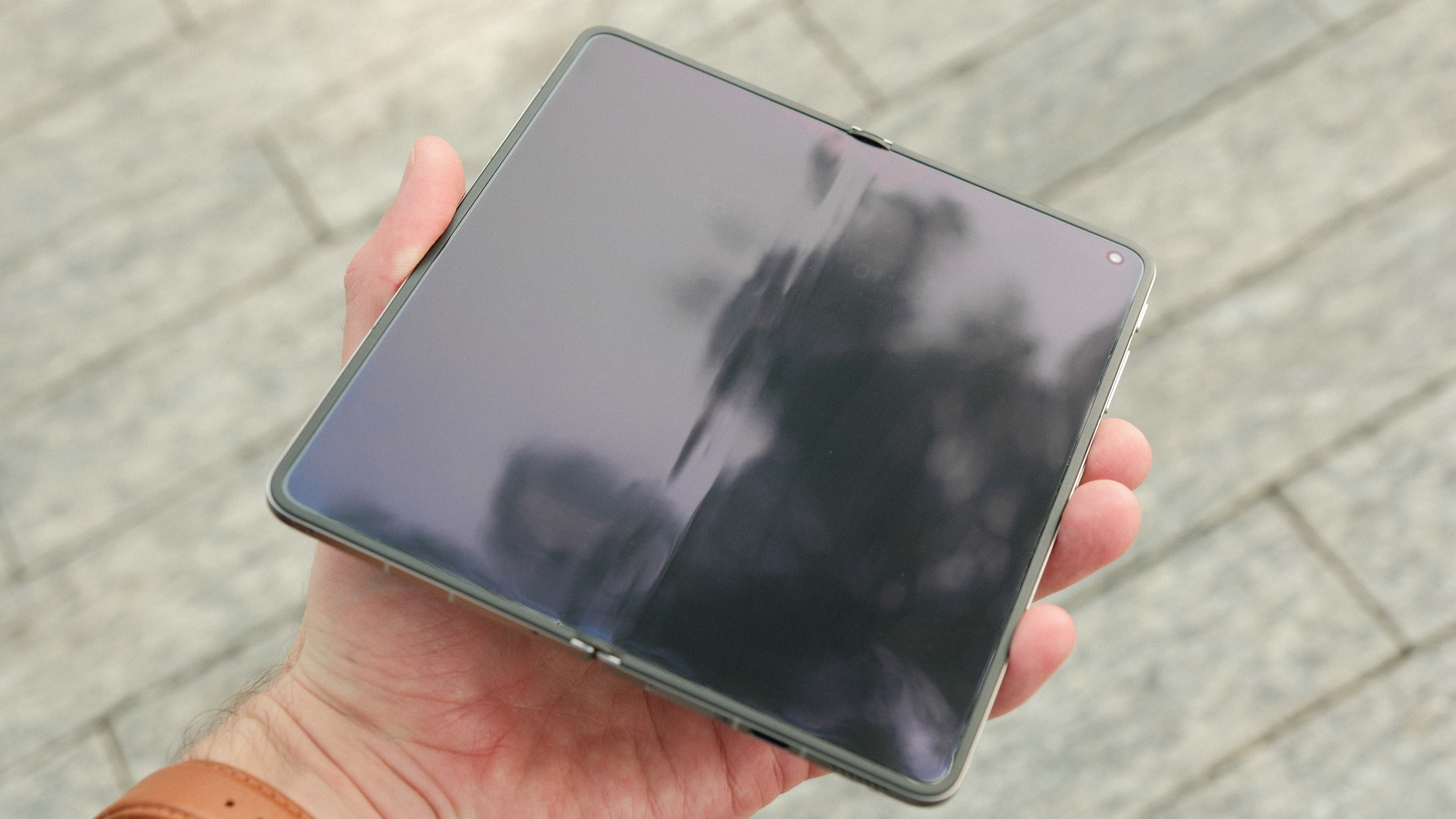 A person holding the Oppo Find N6 fully unfolded, showcasing the large, nearly square internal tablet-sized display. The screen is dark, reflecting the surrounding environment.