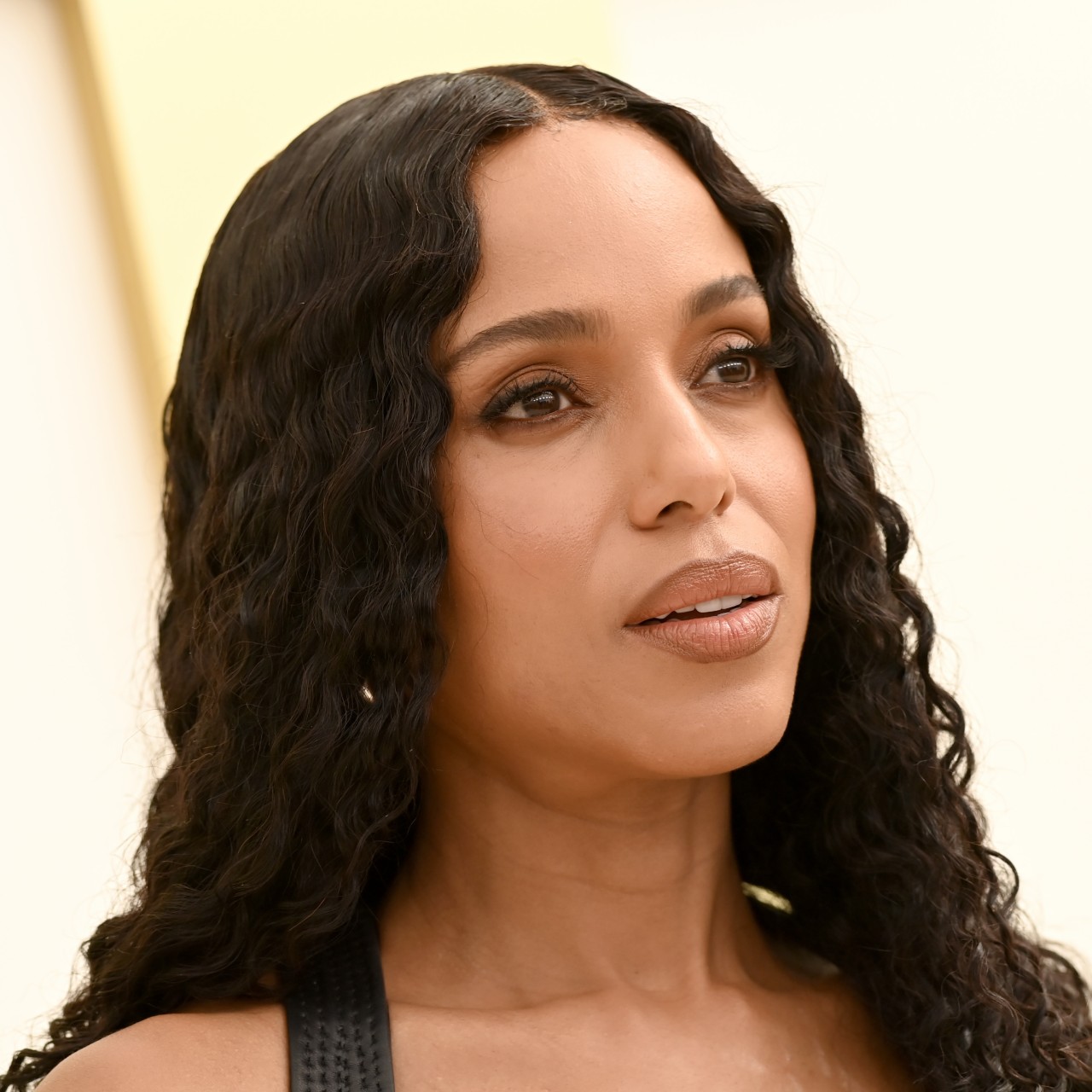 a black woman with long, curly hair poses in front of a cream background