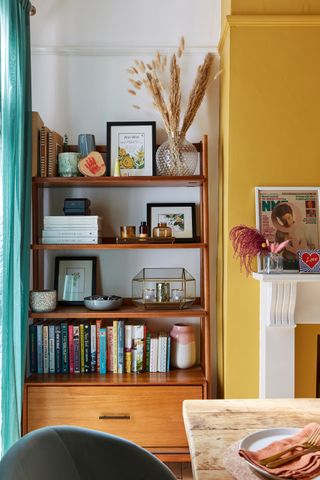 wooden mid century shelving unit in a dining room with a mustard yellow feature wall