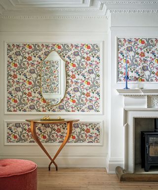 Living room with white painted walls, floral wallpaper framed by paneling, fireplace, console table