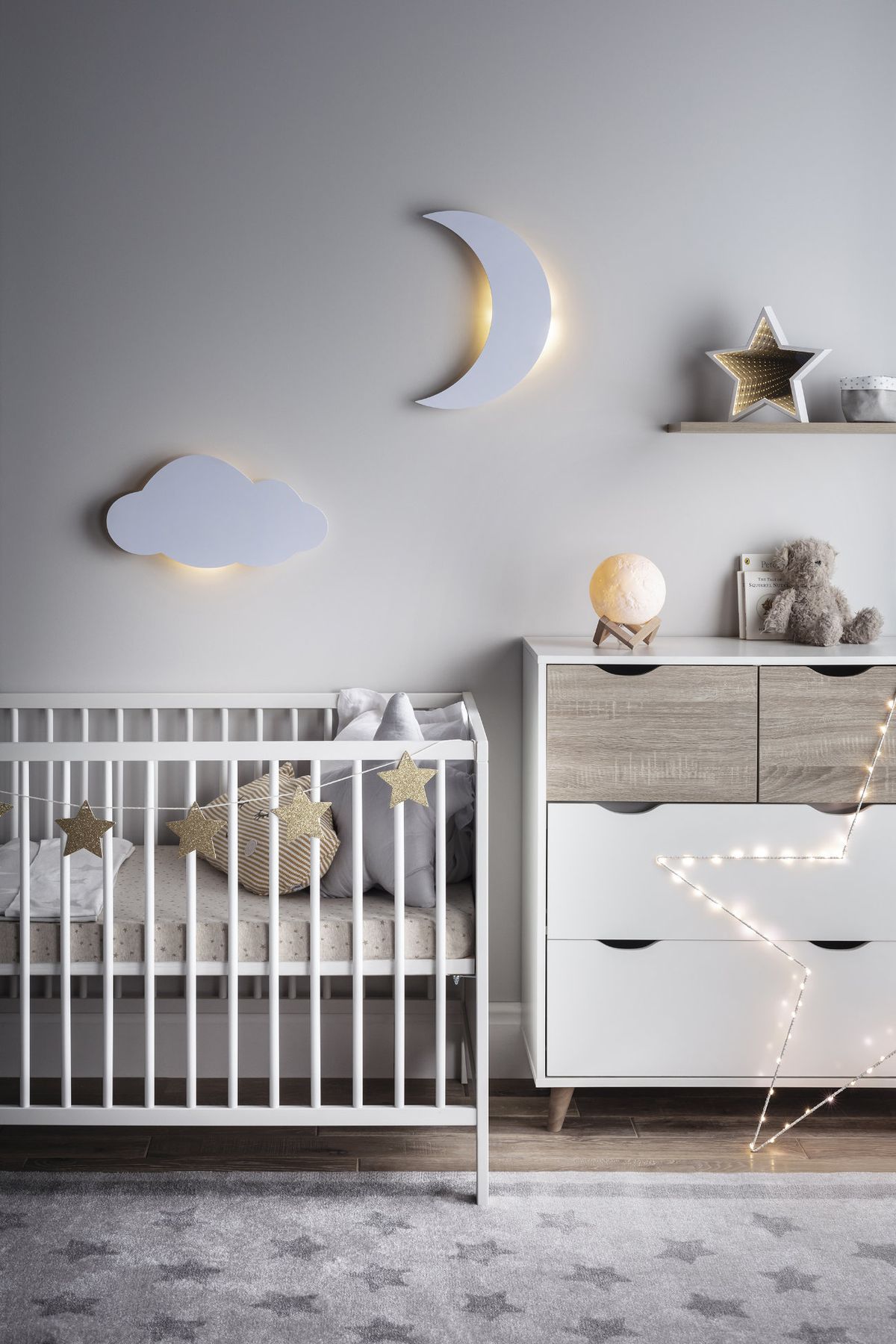 A children's bedroom decorated in white hues with a crib and styled lighting fixtures shaped like a crescent moon and a cloud