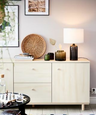 Pale wooden sideboard with a lamp, vases and a pile of books on the surface