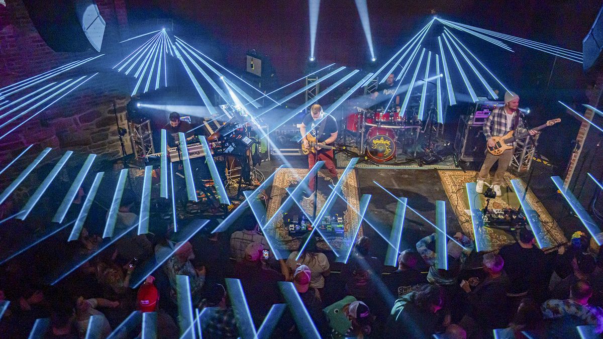 The stage is alit with blue lasers as a bands rocks out. 