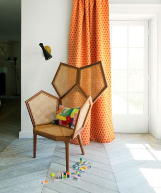 A mid-century modern living room with rattan chair, orange drape and white walls.