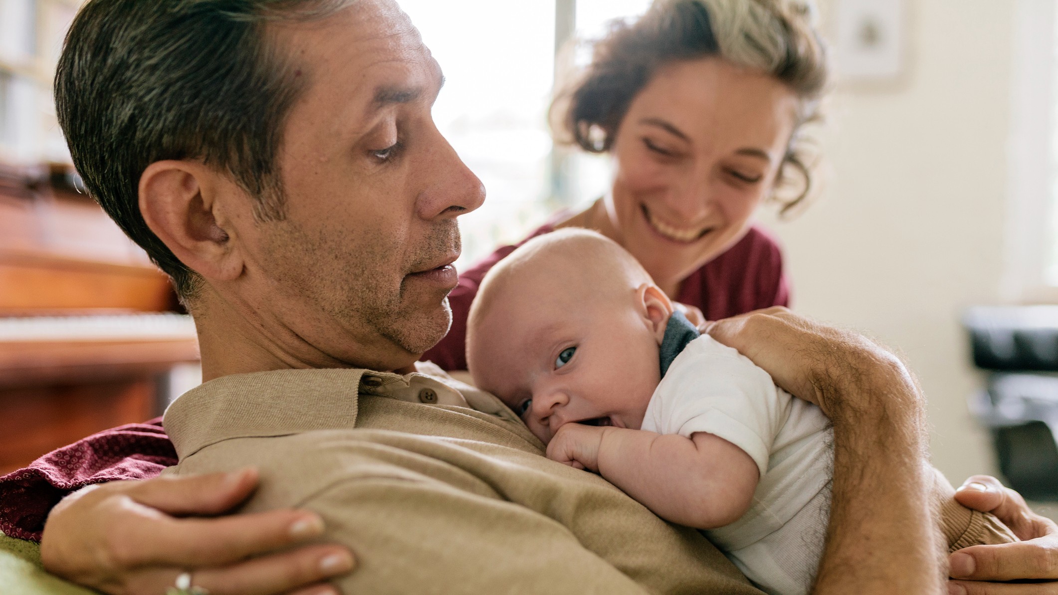 Close-up of proud grandparents embracing newborn. Couple is sitting on livingroom couch. They are in their 50s and fairly young to be grandparents.