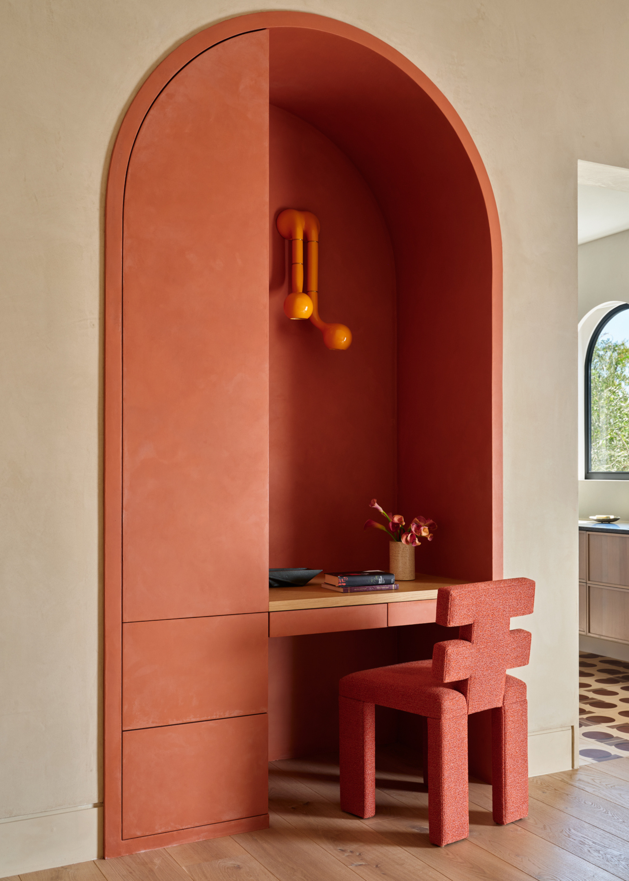 A study space with limewash orange walls, a structural sconce, a peachy orange chair, and a floating desk