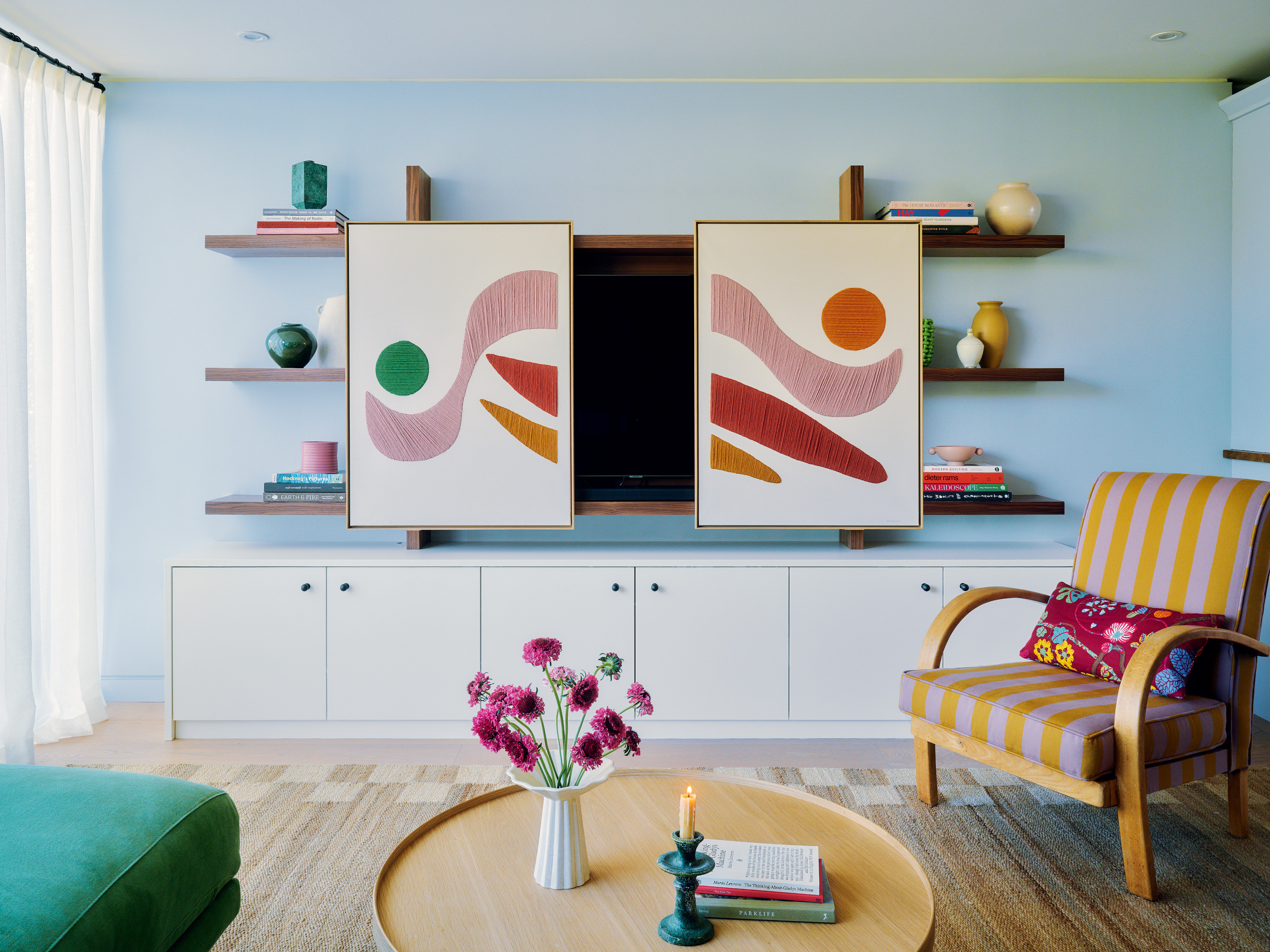 Blue living room with abstract artwork covering TV, striped orange and purple armchair and round light wood table