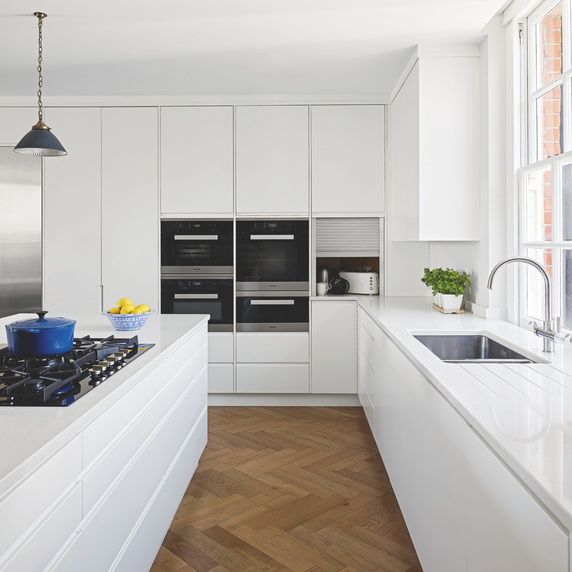 Modern white kitchen units floor to ceiling, with gas hob in the kitchen island and parquet flooring.