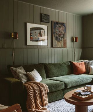 A green couch in a green living room with a gallery wall